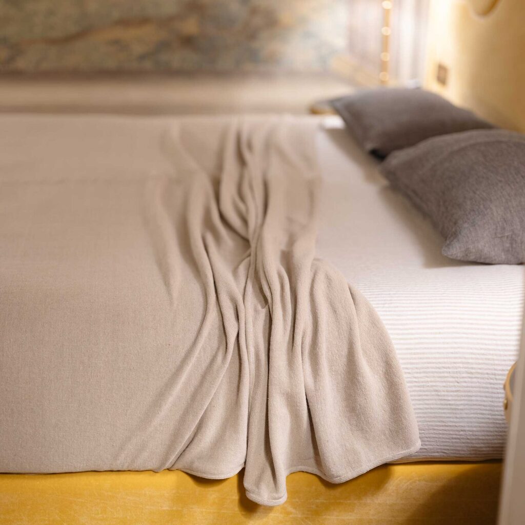 A tan Rawganique blanket on top of the brand’s sheets and a colorful bed frame