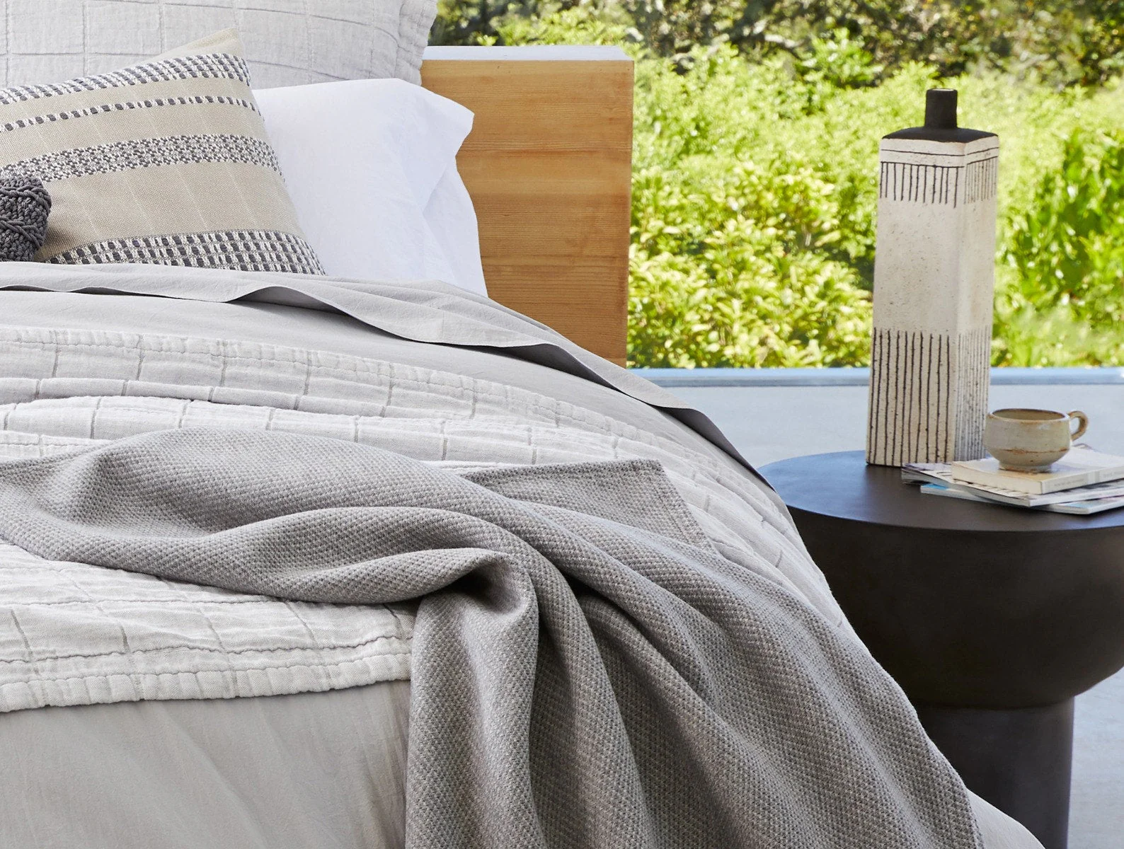 A gray wool blanket on top of a bed with light gray bedding