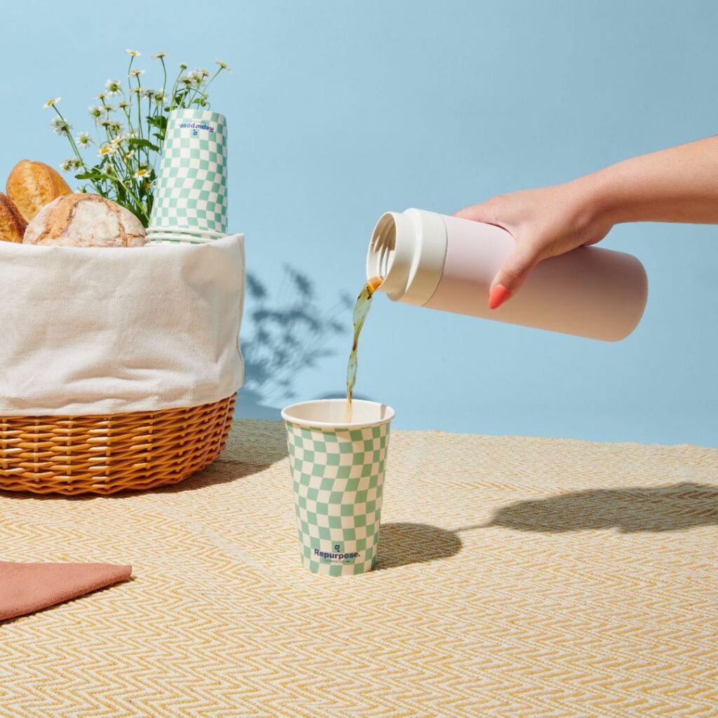 A woman’s hand pouring coffee from a thermos into a compostable cup