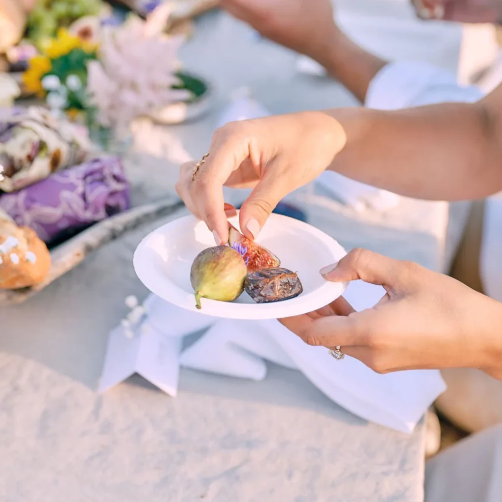 A close-up of a woman holding a small compostable plate with figs on top