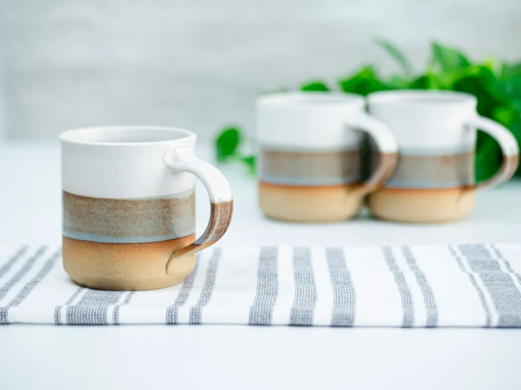 An assortment of lead-free ceramic mugs with blue, brown, and off-white stripes sit on a table