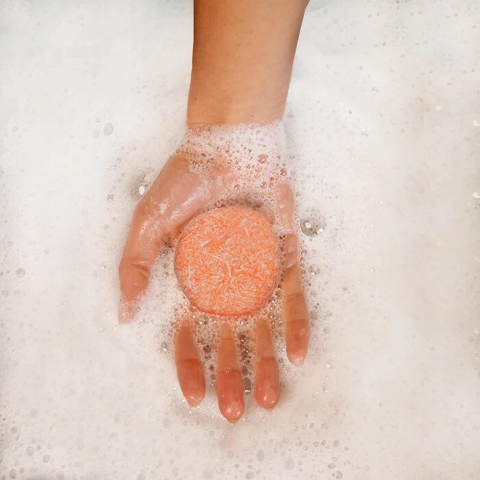 A hand holding an orange bar of natural shampoo from Seek Bamboo