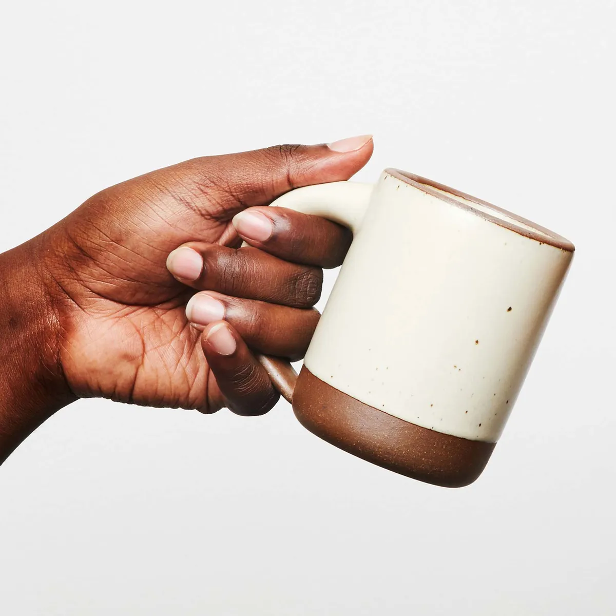 A hand holding a cream and brown ceramic mug from East Fork