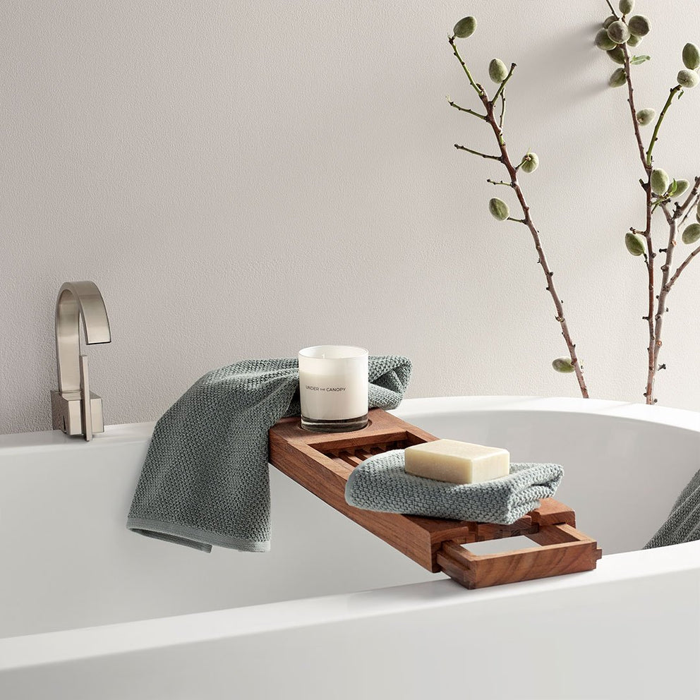 Wooden tray on bath with towels, soap, and candle