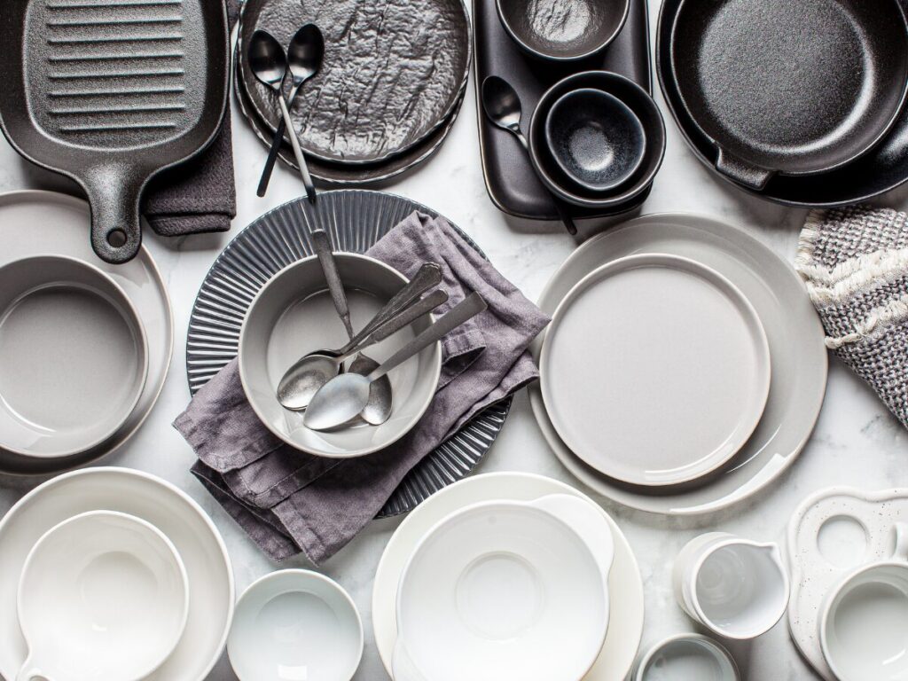 A collection of steel bakeware, stainless steel cookware, and ceramic cookware sitting on a white tabletop