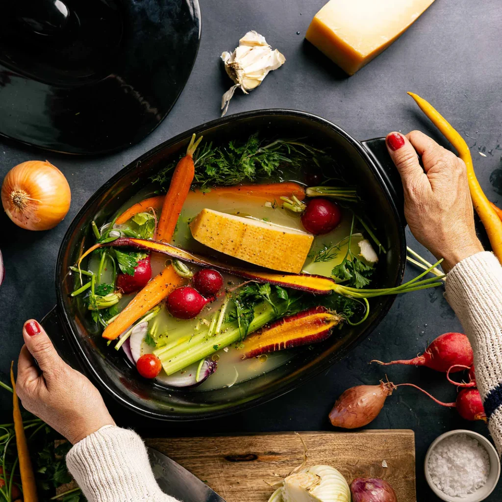 Two hands holding an Xtrema Dutch oven filled with vegetables and broth