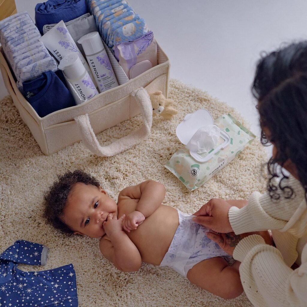 A mother puts a fresh diaper on a baby after wiping the baby with PFAS-free baby wipes.