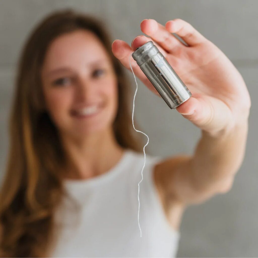 A woman holding a stainless steel container of TreeBird PFAS-free floss