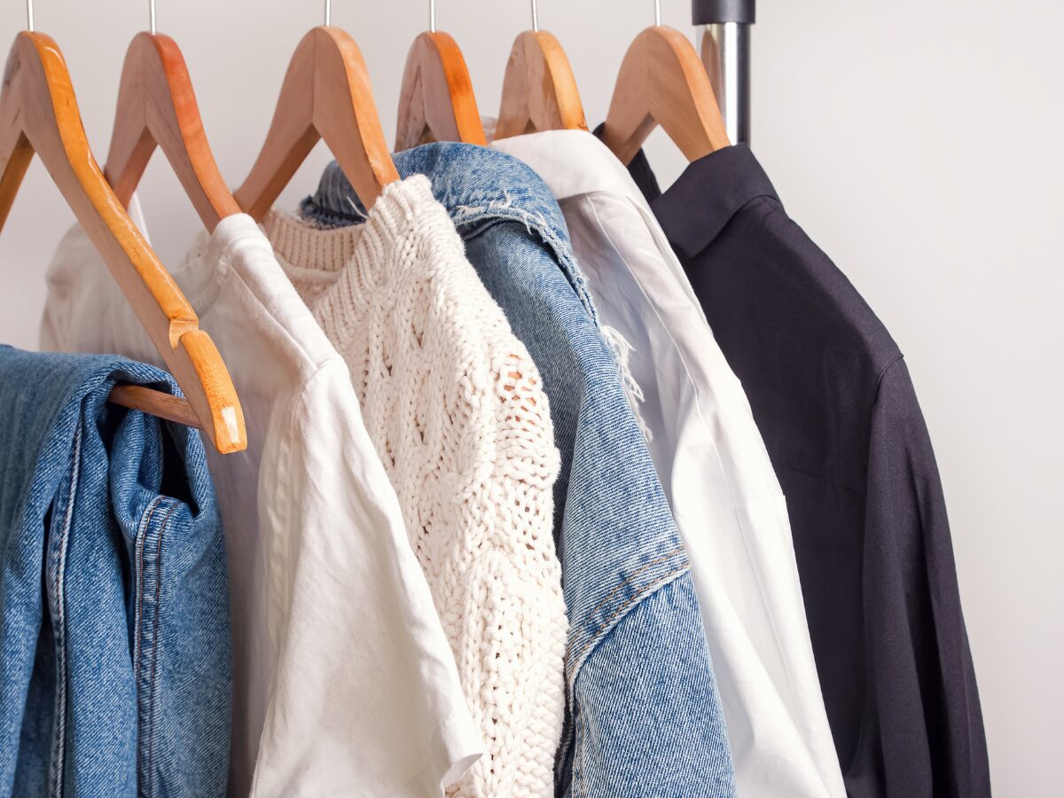 Various clothing items, including jeans, a denim jacket, and a white sweater, sit on hangers.