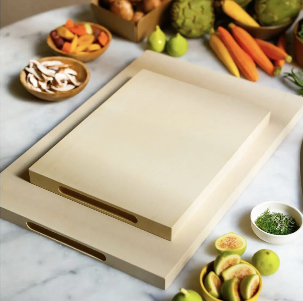 Two cream-colored rubber cutting boards stacked on top of a countertop filled with fresh fruit and vegetables