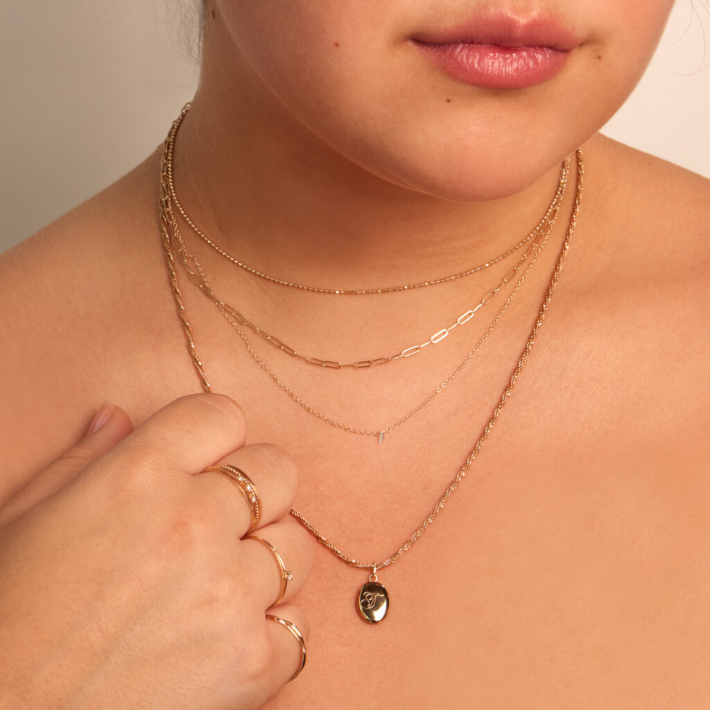 A woman wearing several simple gold necklaces and a gold pendant with a T on it