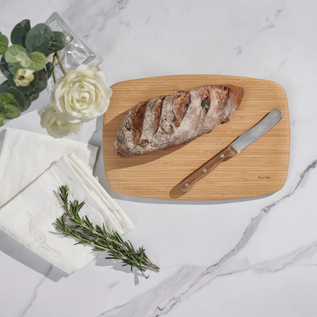 A loaf of bread and a knife on a bamboo cutting board and white marble countertop.