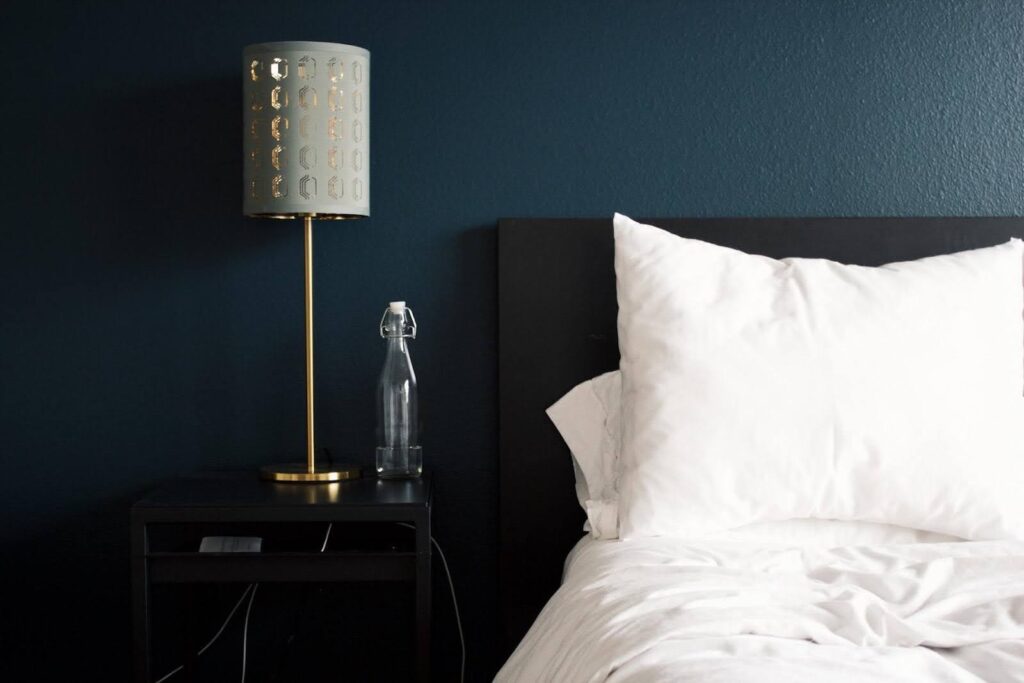 White pillow and blanket on a bed next to a table with a gold lamp