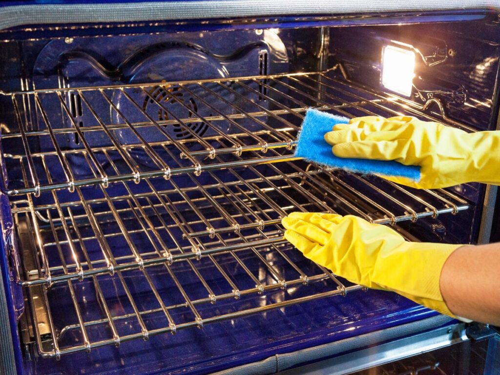 Two hands with yellow gloves cleaning an oven with a sponge